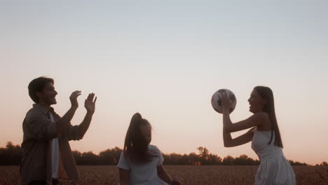 family playing soccer in a wheat field at sunset