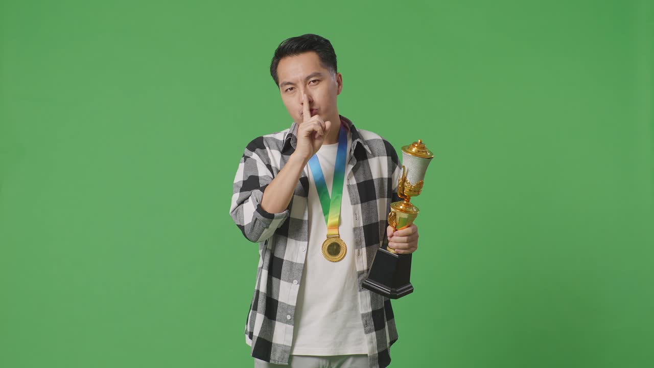 입술 에 손가락 을 고 트로피 와 메달 을 들고 있는 사람