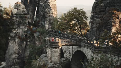 close up view on the bastion bridge in saxony germany near dresden while people explore the place during sunset. the bridge is build into stunning rocks what makes it a big tourist attraction
