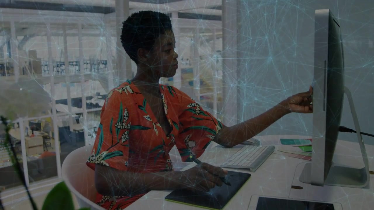 Vertical video: Glancing at screen, artist in orange checking swatch to screen with stylus at desk