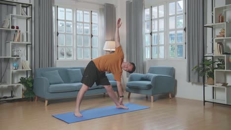 hombre asiático haciendo yoga en postura triangular en la alfombra en casa