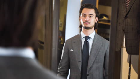 Mirror-reflection-of-young-man-trying-on-suit-in-fashion-boutique