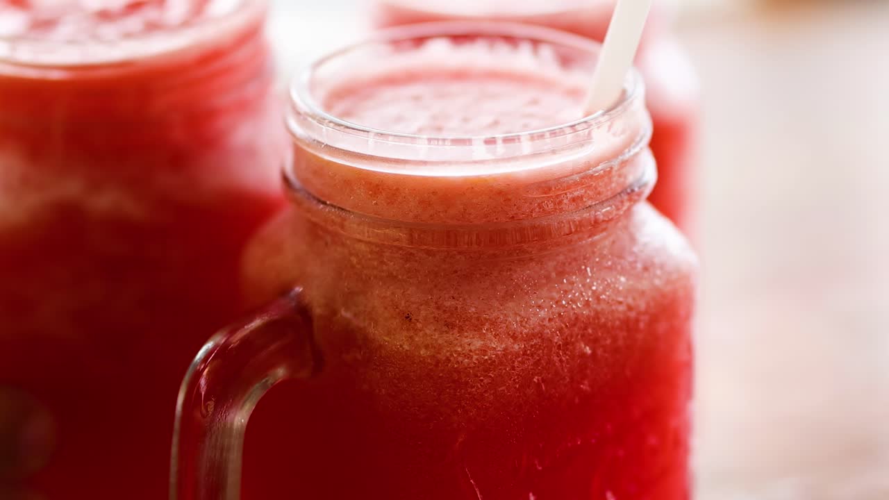 A detailed view of refreshing watermelon juice served in glass mugs with handles and straws.