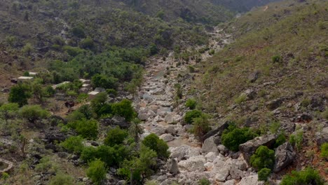 Aerial-view-of-the-dry-riverbed-with-huge-boulders-and-a-small-village-standing-nearby