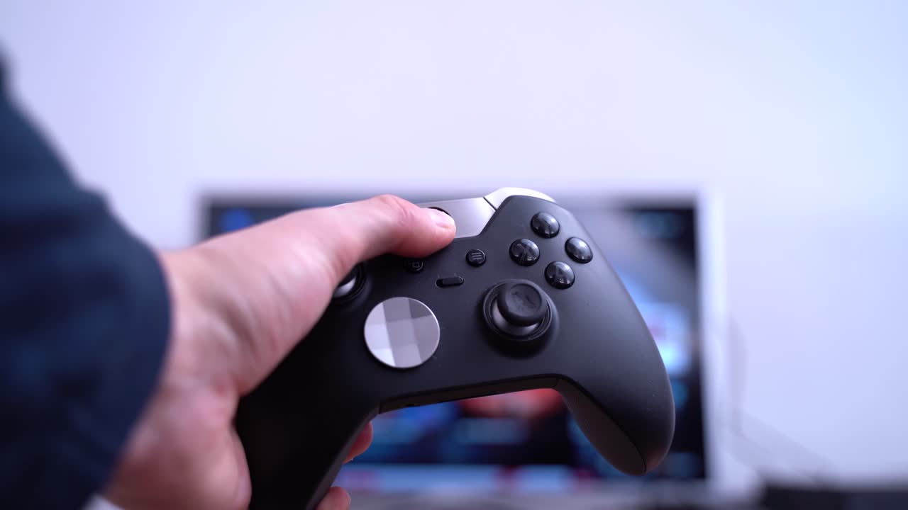 Hand holding an Xbox One Elite Controller, turning it on, then focus on tv