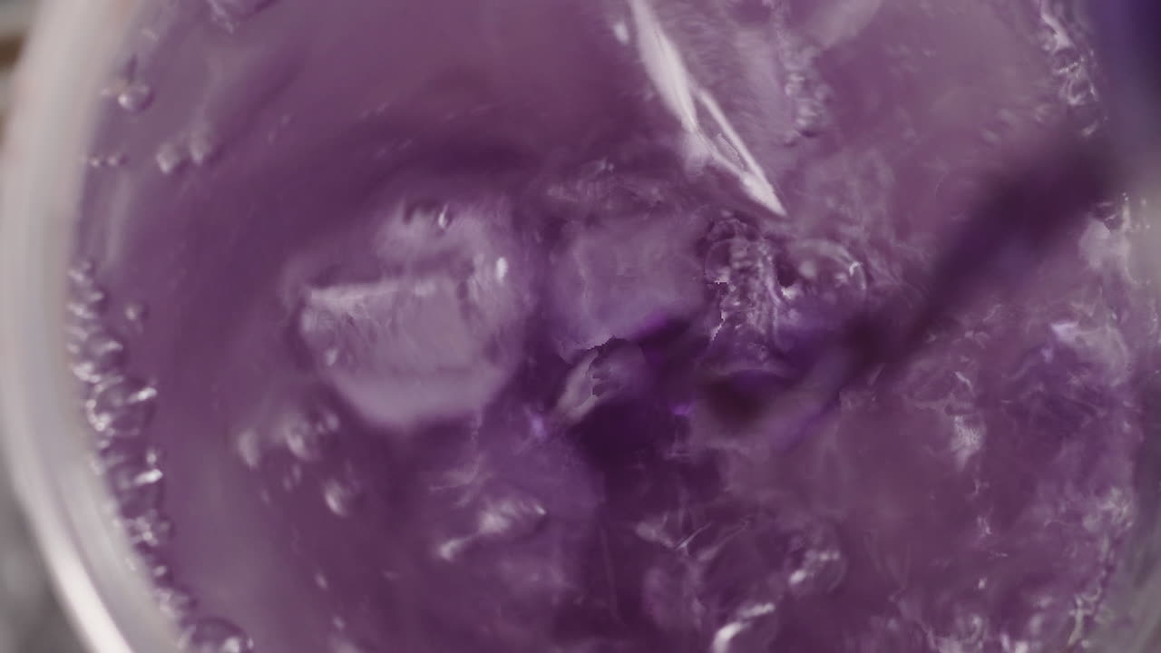 Bovenaanzicht, stroom paars sap dat in een glas water met ijs wordt gegoten