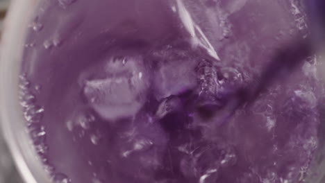 vista de arriba hacia abajo, chorro de jugo morado que se vierte en un vaso de agua con hielo