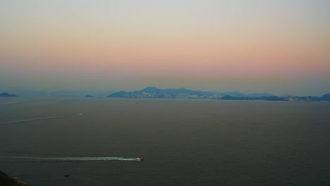 drone shot of the sea during a very polluted day, the sun barely go through the atmosphere. some boat are passing by and there is an island in the distance.