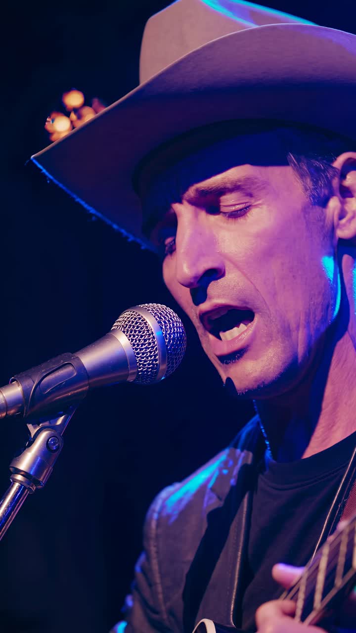 Low-angle video of a musician in a cowboy hat playing guitar, focused on the microphone, with moody
