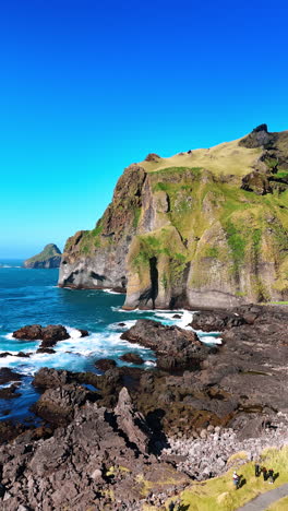 steep cliff and smaller rocks at the shore of iceland. water splashes by the rocks creating white foam. vertical video.