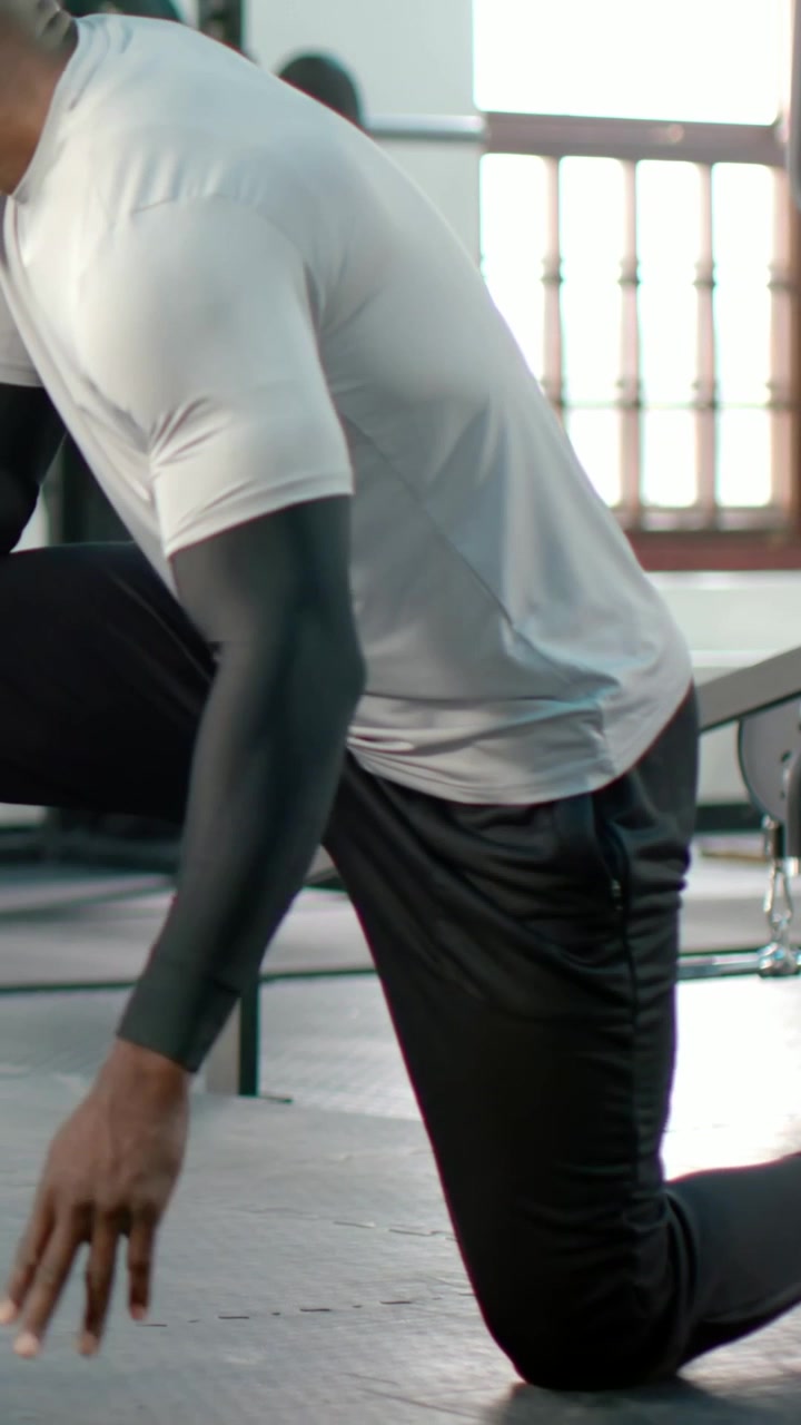 Vertical video: Man lowering rear knee doing kneeling lunge for hip stretch at gym bench in sleeves