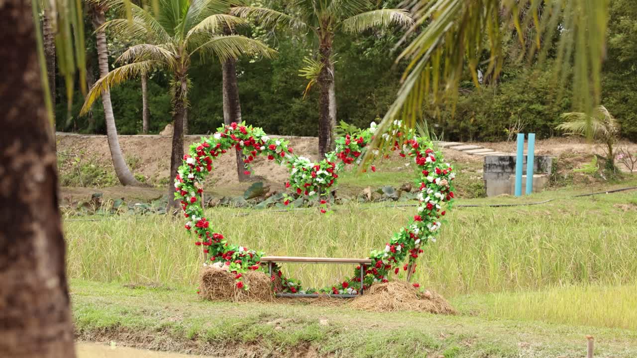 A heart-shaped floral frame stands in a lush, tropical setting with gentle camera movement and natural lighting