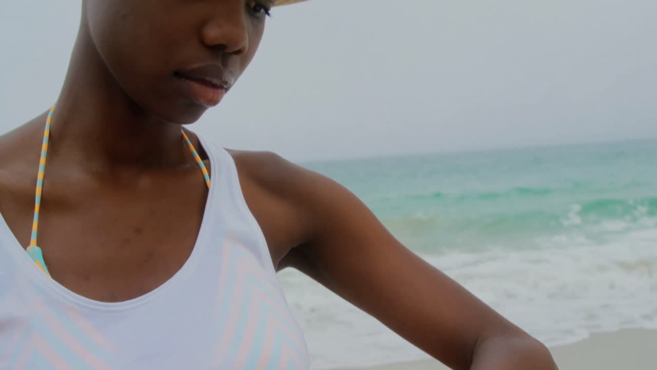 Front view of African american woman using smartwatch on the beach 4k