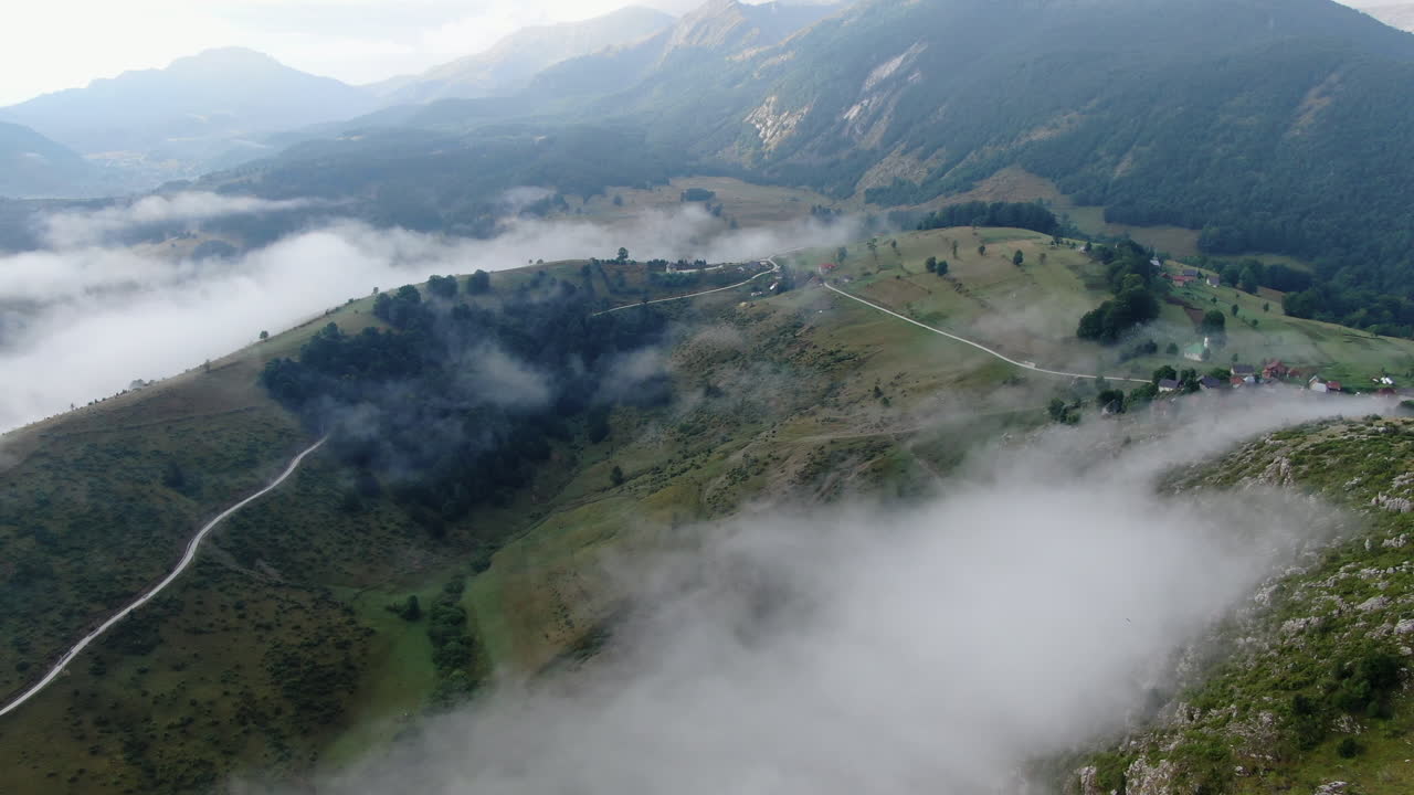 A landscape aerial view shows hills with some trees White clouds fill valleys between the hills A road runs across the side of one of the hills