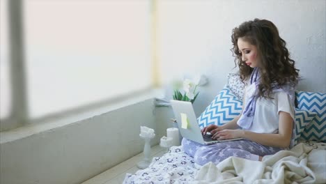 young woman working on laptop in cozy bedroom
