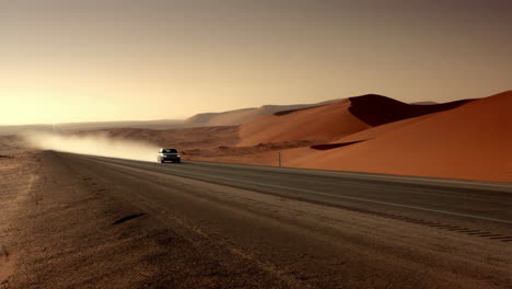 car driving on a desert road through sand dunes