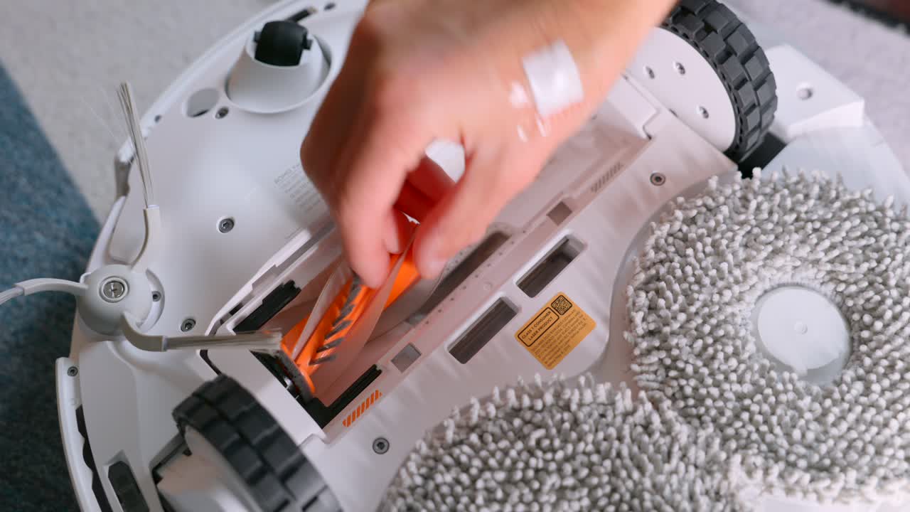 Nærbillede af undersiden af en hvid robotstøvsuger, der viser børsterullerne og moppepuderne
