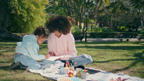 creative family drawing picnic at green sunny lawn. mom child painting