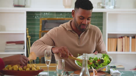 man enjoying festive meal, serving salad at diverse family christmas dinner table