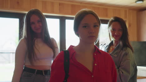 three young girls pose indoors near window in wooden cabin as lady in sunglasses begins to remove them with confident expression, warm light creating cozy mood and stylish casual atmosphere