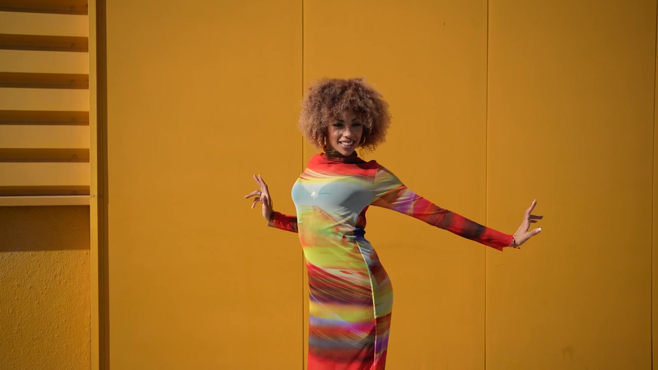 A vibrant woman joyfully dancing in front of a bright yellow wall radiating energy and happiness