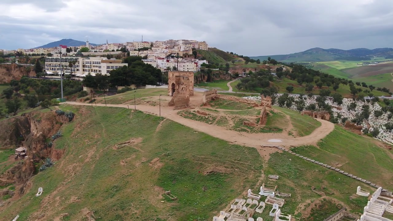 Vista aerea con drone di rovine storiche circondate da verdi colline e paesaggio rurale a Fez, Marocco, ideale per documentari di viaggio e progetti culturali.