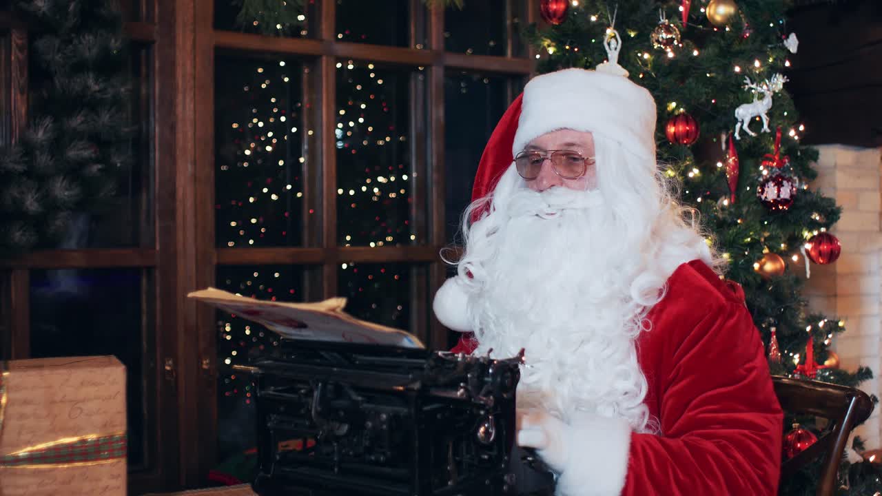 Santa Claus writes a letter at a typewriter, sitting in an evening room near a Christmas tree