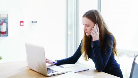 business executive writing on diary while talking on mobile phone