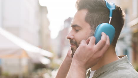 joven feliz con auriculares inalámbricos eligiendo, escuchando música bailando al aire libre en la calle de la ciudad