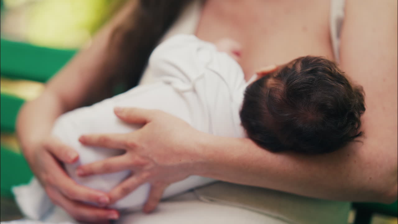 Tender moment of a mother breastfeeding her baby while sitting on a park bench