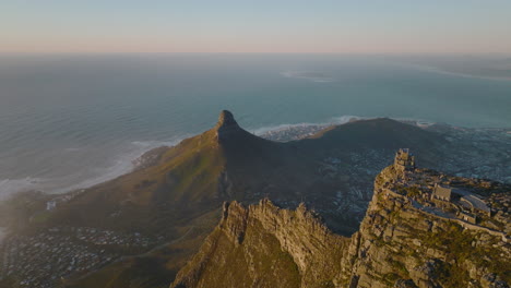 Slide-and-pan-aerial-footage-of-pointed-Lions-Head-mountain-above-sea-coast.-Fly-over-Table-mountain-and-revealing-houses-in-urban-neighbourhood.-Cape-Town,-South-Africa