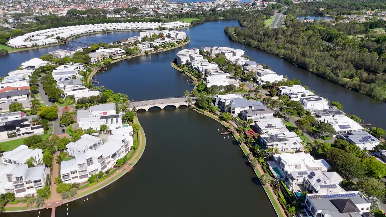 Sunny aerial flyover of modern waterfront residential community, curving canal, bridge, and greenery