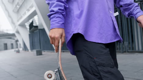 hombre con una tabla en la mano afuera. hipster irreconocible caminando por la calle de la ciudad.