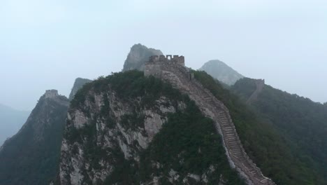 Fly-over-old-part-of-Great-Wall-of-China-with-deteriorate-lookout-tower-on-top-of-mountain-on-a-cloudy-day
