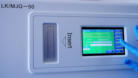 Touch screen panel switched on at the equipment for sterilization. Gloved hand of medic presses keys to start the procedure of disinfection.