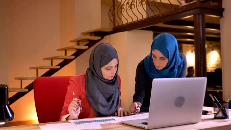 closeup portrait of young muslim female employee and employer discussing the data on the graph in front of the laptop. boss pointing out on the mistakes found in work of younger office worker