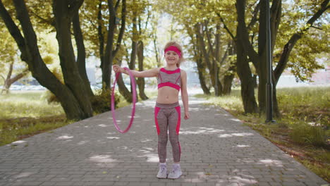 Athletic-fitness-children-girl-training-playing-twisting-Hula-hoop-circle-ring-on-hand-in-park