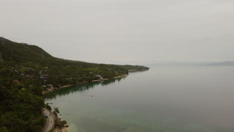 Aerial-footage-revealing-a-street-on-the-waterfront-with-houses-and-a-tropical-forest-in-the-back-in-Cebu-Philippines,-Asia,-Drone