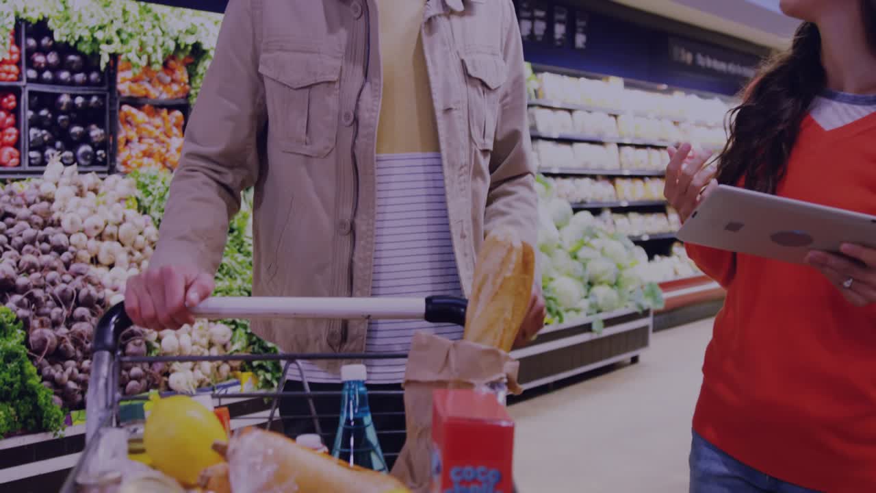 Couple pushing cart in grocery woman holding tablet reaching touching arm resting leaning smiling