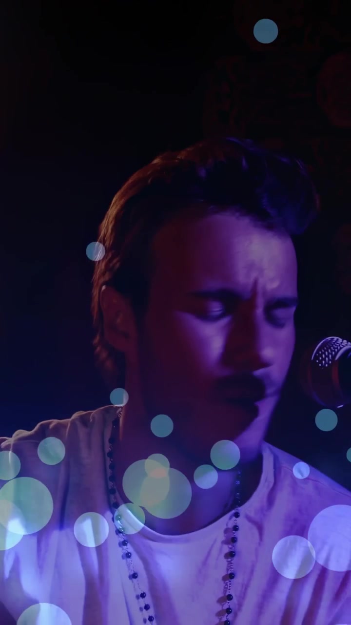 Vertical video: Male musician opening eyes on cue, performing into mic, bokeh drifting over face