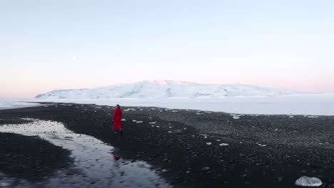 Antenne:-Herumfliegende-Person,-Die-Am-Schwarzen-Strand-Mit-Weißem-Arktischem-Schnee-In-Island-Im-Winter-Schnee,-Eis,-Wellen,-Wasser-Geht