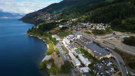 aerial backward moving shot over queenstown township and center along the majestic mountain slope beside a lake in new zelaand at daytime