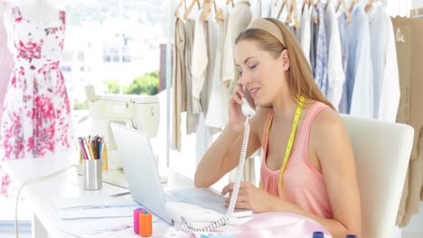 diseñadora de moda atractiva trabajando en una computadora portátil y contestando el teléfono
