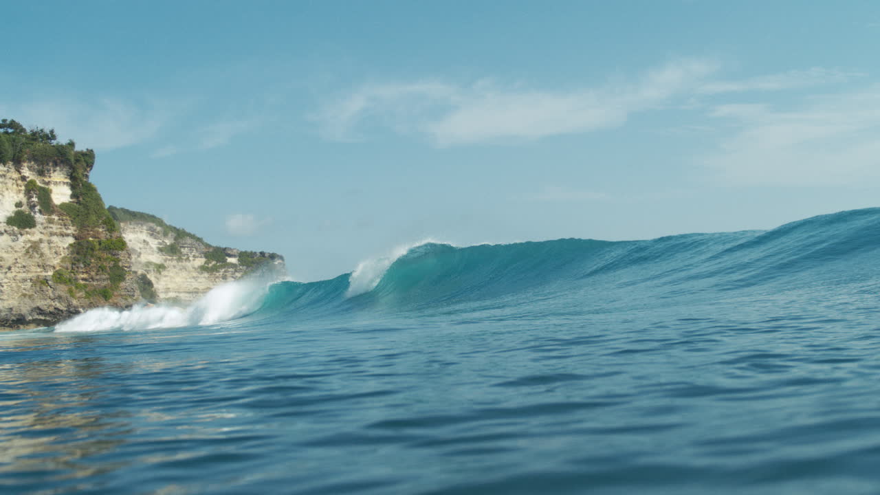Wave breaks gently near rocky coastline in smooth ocean slow motion