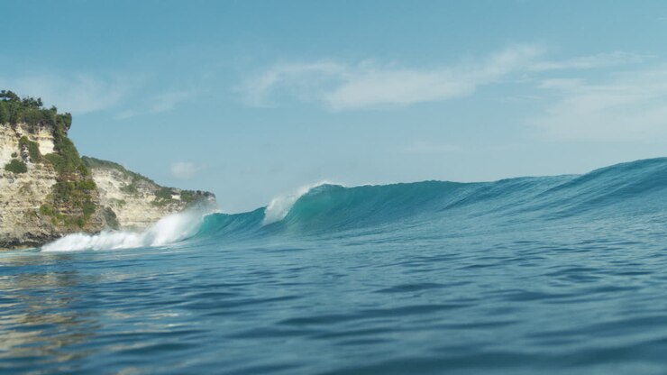 Wave breaks gently near rocky coastline in smooth ocean slow motion