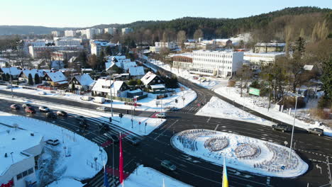 cars waiting and driving on black asphalt for a traffic light which turned green on a roundabout on a cold sunny winter day with multiple vlags slowly flapping in the wind