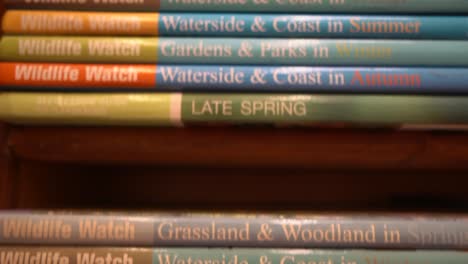 Toma-De-Seguimiento-De-Primer-Plano-De-Pilas-De-Volúmenes-De-Libros-De-Observación-De-Vida-Silvestre-En-El-Estante-De-Madera