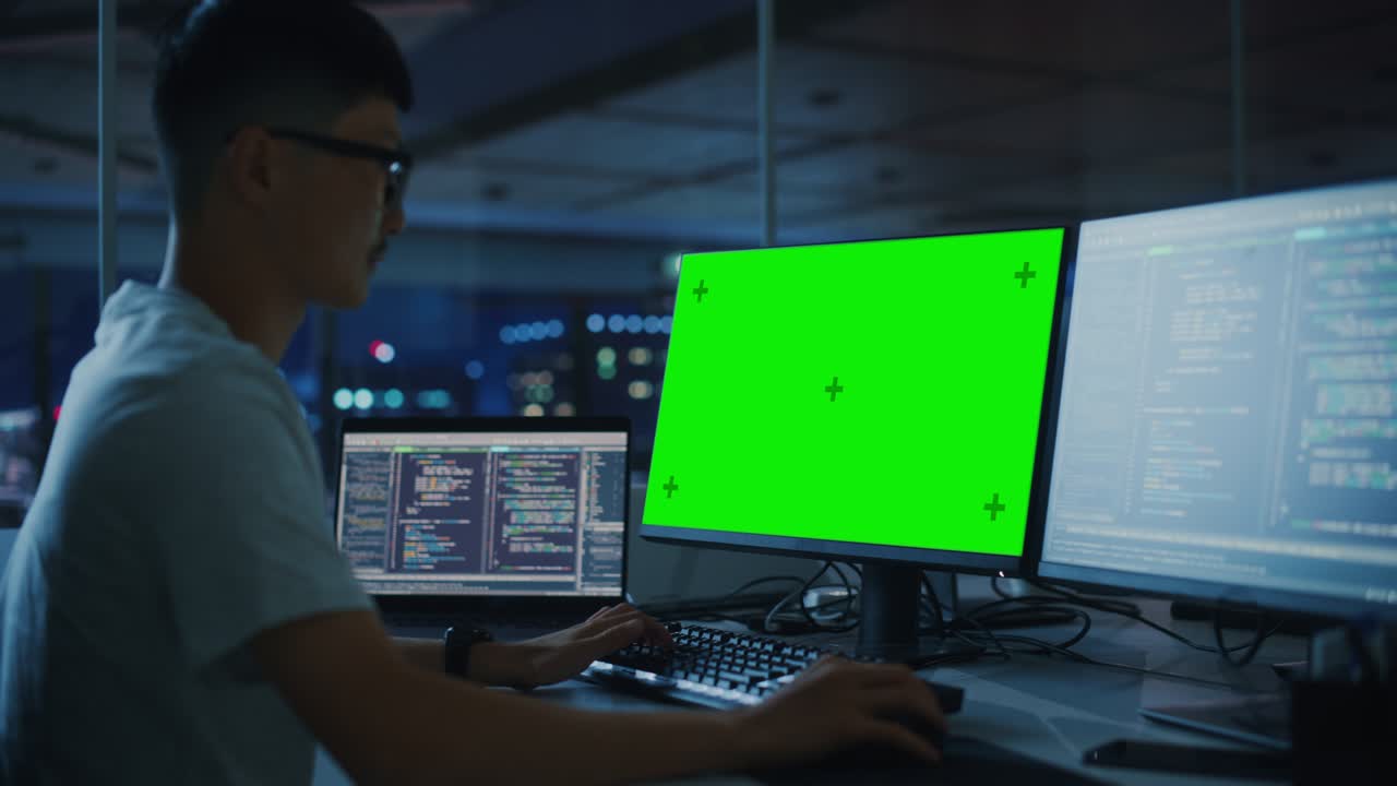 oficina nocturna: joven japonés trabajando en una computadora de escritorio de pantalla verde. equipo de programadores escribiendo código, creando software moderno, diseño de aplicaciones de comercio electrónico, programación de negocios electrónicos