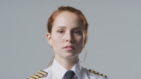 studio portrait of serious female airline pilot or ship captain against plain background