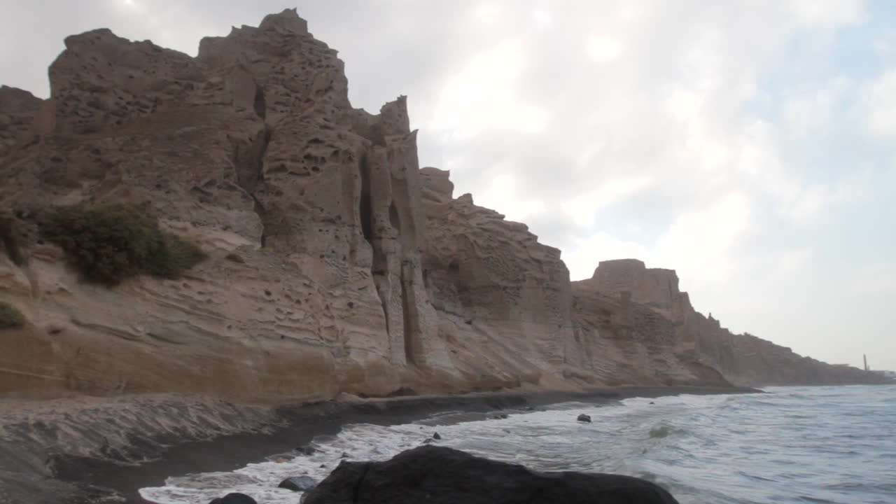 Tracking shot of a black beach with white volcanic cliff formations getting hit by big waves